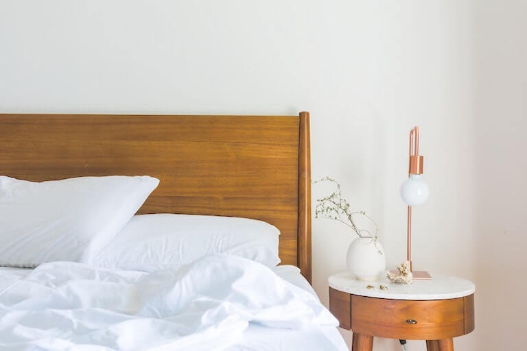 White Bedspread Beside Nightstand With White and Copper Table Lamp
